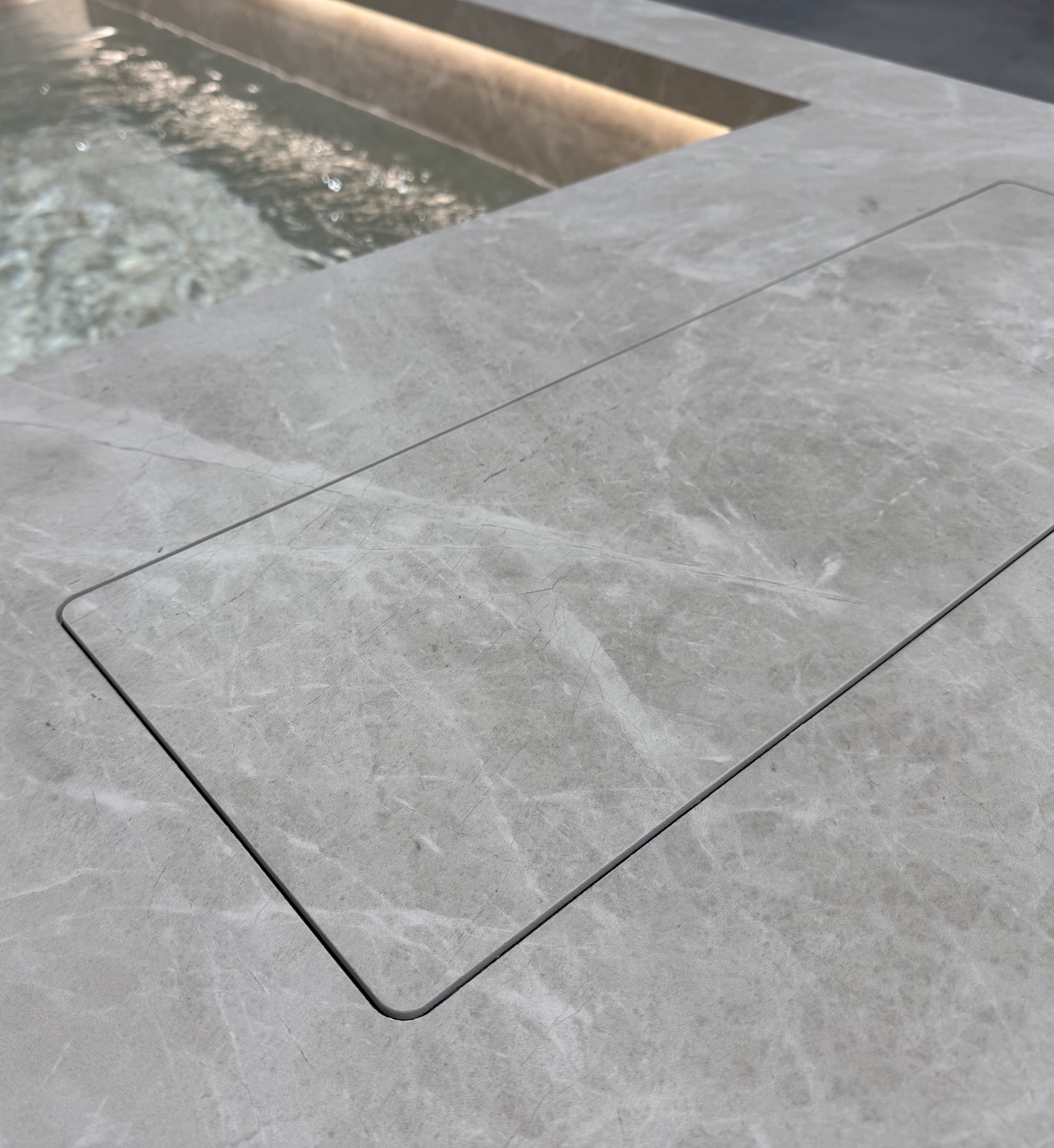 Close-up of Laminam stone deck surrounding an integrated water feature, showing the seamless stone joint and subtle marbling